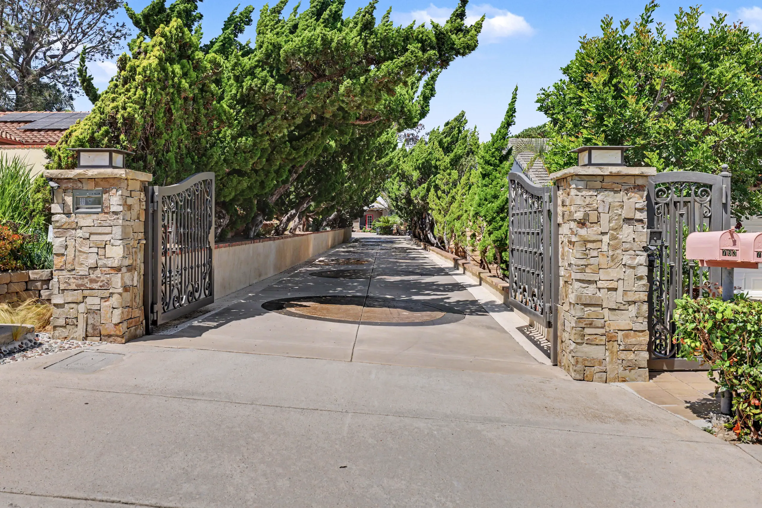 Stone pillars and iron gates at the head of the private drive, framed by mature cypress.