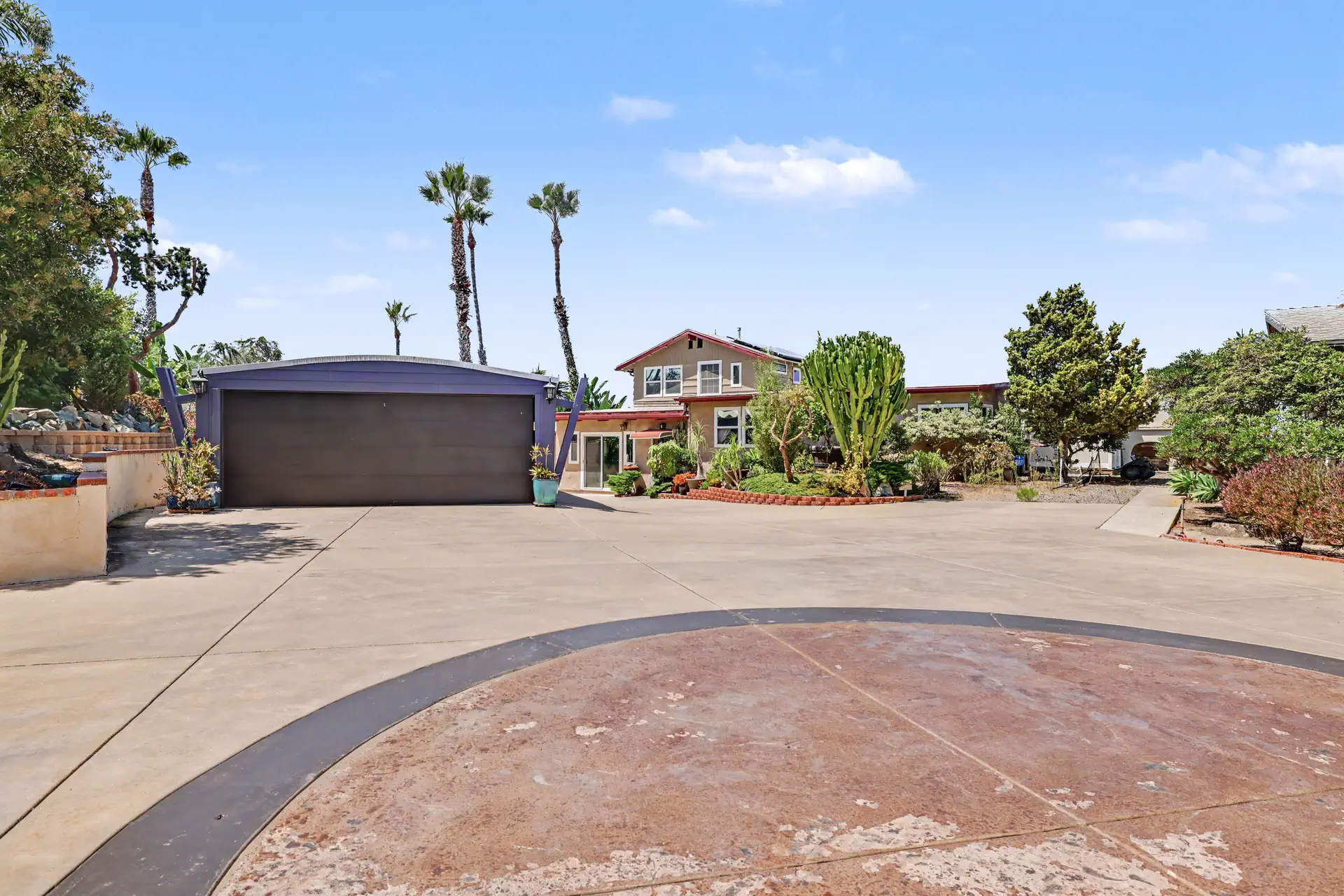 Broad concrete motor court with the detached garage at left and the main residence beyond.