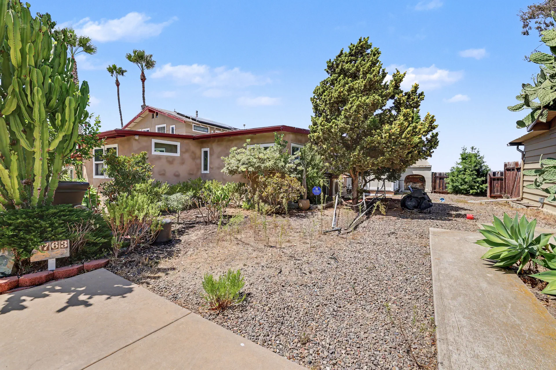An existing residence above a graded yard planted with mature cactus.